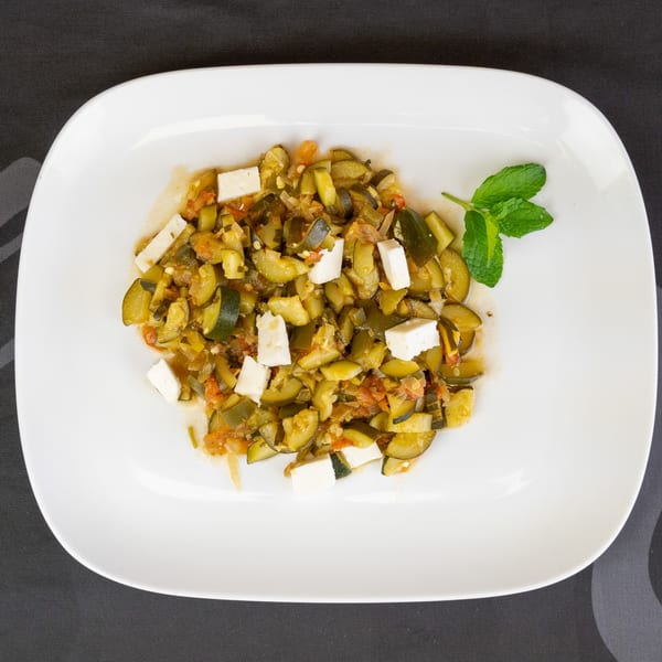 Sautéed zucchini and tomatoes with feta cheese and a mint garnish on a white plate.