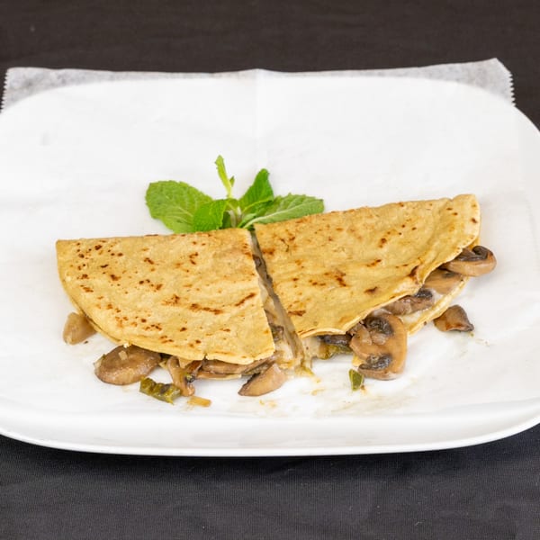 Mushroom and cheese quesadilla, cut in half, garnished with mint on a white plate.