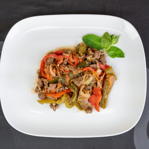 Sizzling beef stir-fry with red and green bell peppers, onions, and fresh mint on a white plate.