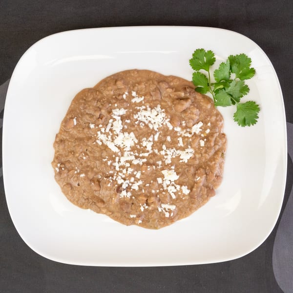 Refried beans topped with crumbled white cheese and a sprig of cilantro on a white plate.