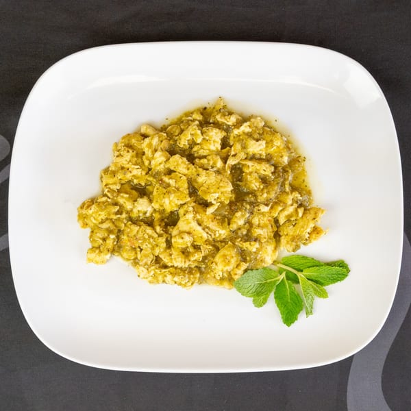 Scrambled eggs with green salsa and a sprig of mint on a white plate.