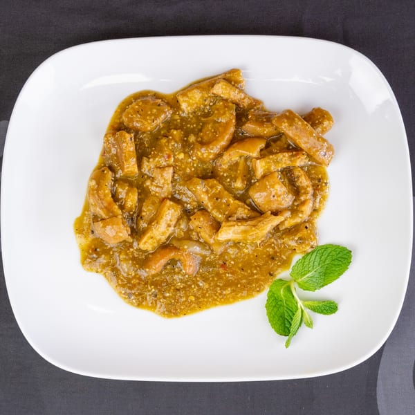 Pork rinds in green salsa, garnished with a sprig of mint on a white plate.