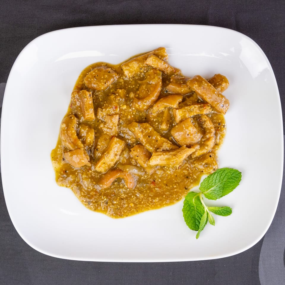 Pork rinds in green salsa, garnished with a sprig of mint on a white plate.