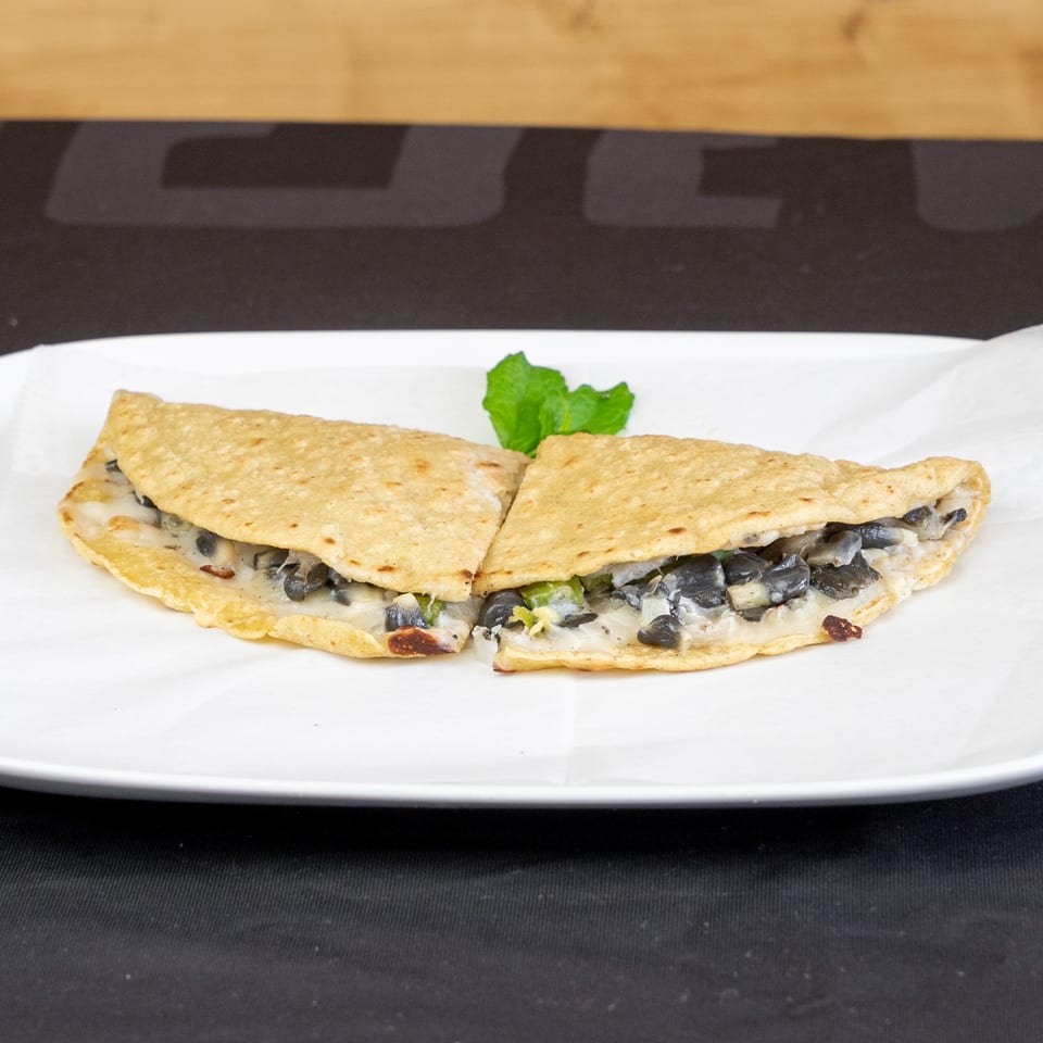 Two quesadilla halves filled with black beans and cheese, garnished with mint on a white plate.
