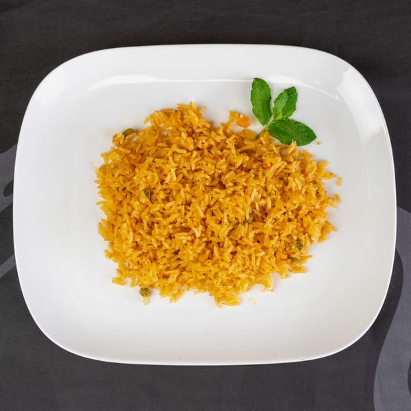 A white rectangular plate holds a serving of golden yellow rice, garnished with a sprig of mint.