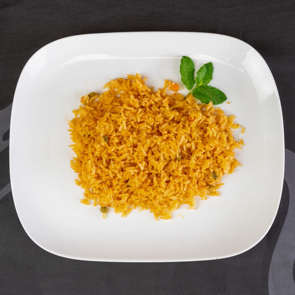 A white rectangular plate holds a serving of golden yellow rice, garnished with a sprig of mint.