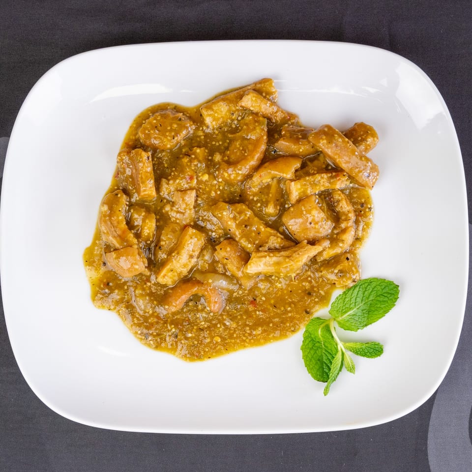 Overhead view of a white plate with green chili stew and a sprig of mint.