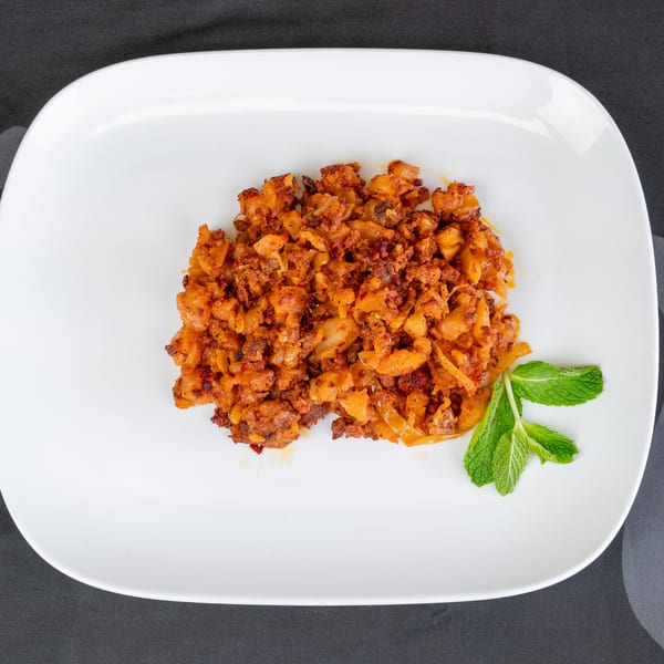Close-up of a white plate with a serving of orange-brown chorizo and potatoes, garnished with mint.