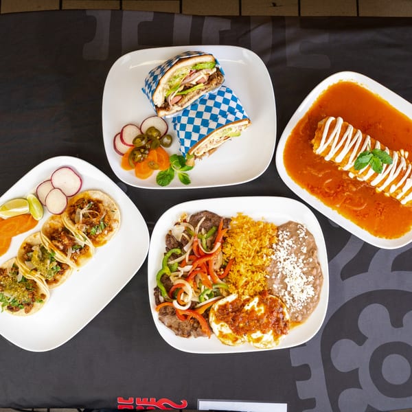 Overhead view of four plates of Mexican food, including tacos, tortas, a burrito, and steak with eggs.