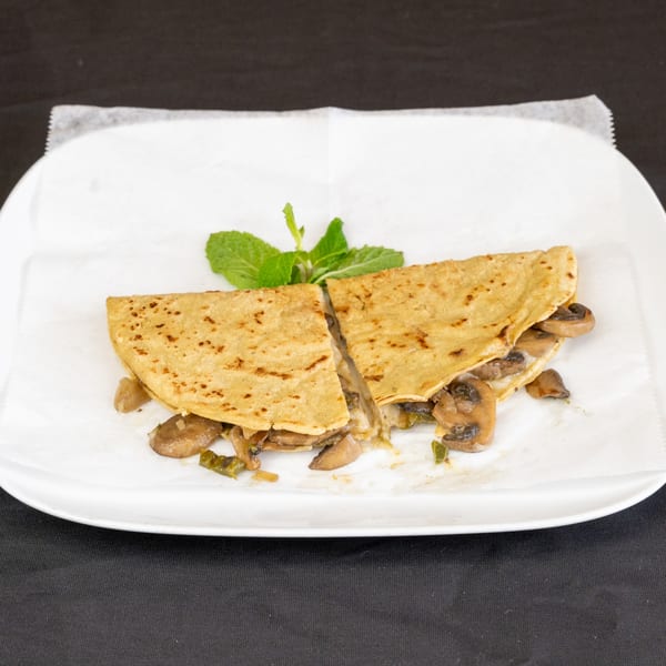 A mushroom and cheese quesadilla, cut in half, garnished with mint on a white plate.