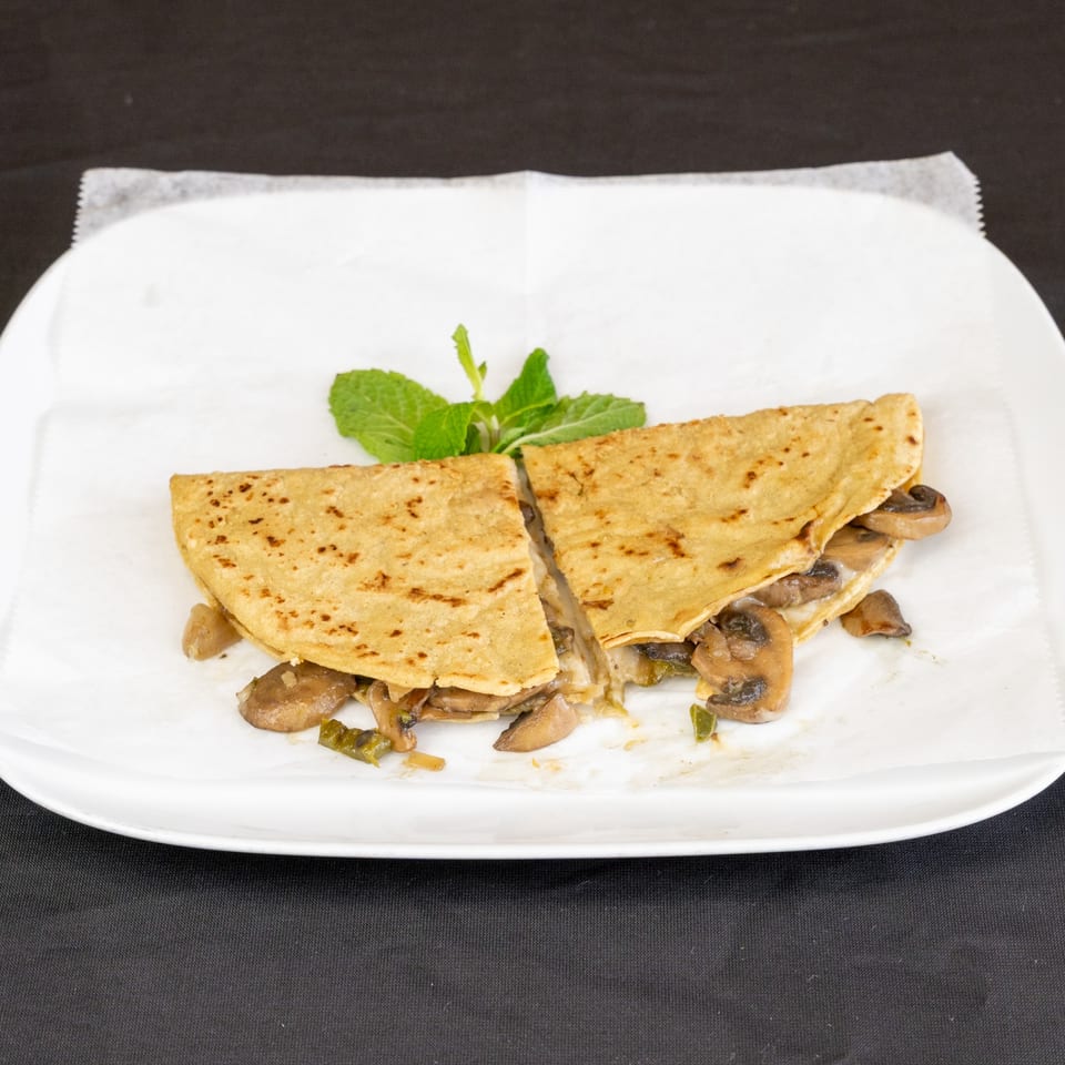 A mushroom and cheese quesadilla, cut in half, garnished with mint on a white plate.