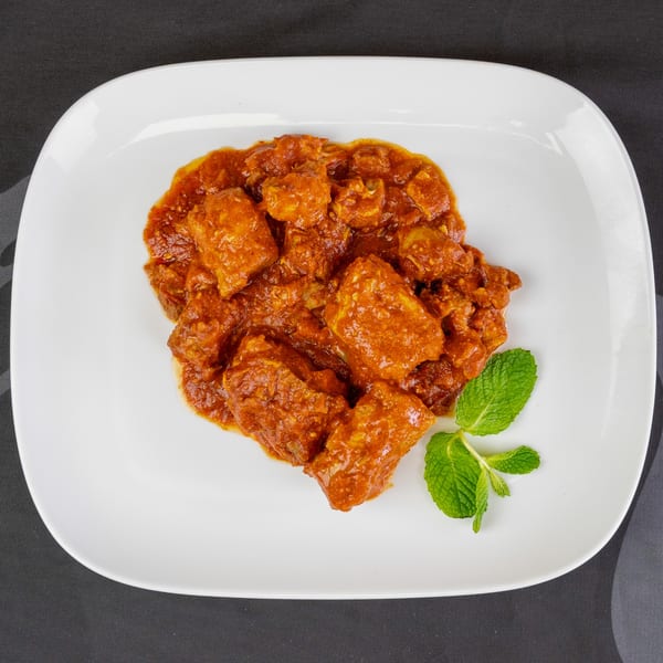 Chicken tikka masala with a sprig of mint on a white rectangular plate.