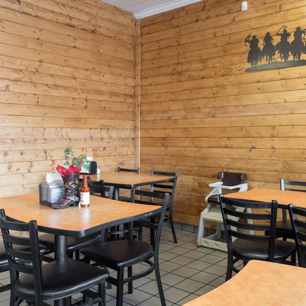 Restaurant interior with wooden paneling, black tables and chairs, and a cowboy boot centerpiece.