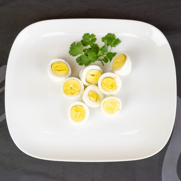 Eight halved hard-boiled eggs with bright yellow yolks and a sprig of cilantro on a white plate.
