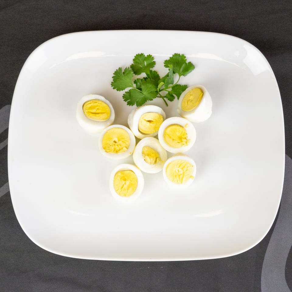 Eight halved hard-boiled eggs with bright yellow yolks and a sprig of cilantro on a white plate.