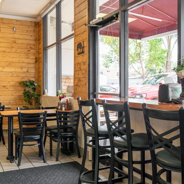 Interior of a restaurant with wooden walls, black tables and chairs, and a window bar overlooking the street.