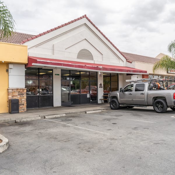Exterior of a restaurant with a red awning, large windows, and a gray pickup truck parked outside.