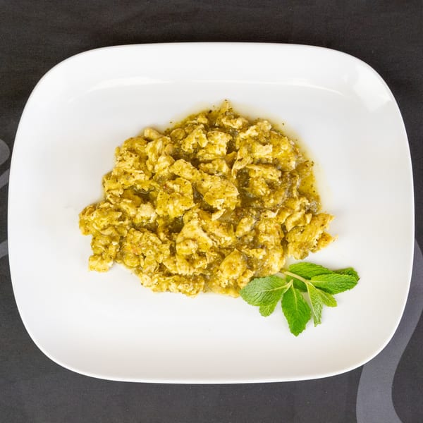 Scrambled eggs with green salsa and a sprig of mint on a white plate.