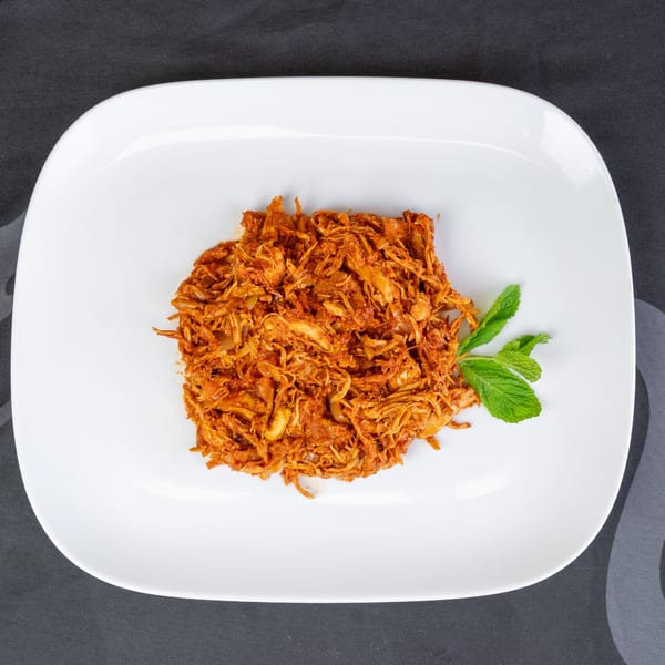 Shredded chicken in a rich red sauce, garnished with fresh mint on a white rectangular plate.