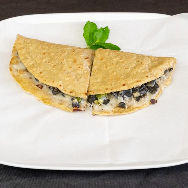 Two halves of a quesadilla filled with black beans, cheese, and green peppers, garnished with mint.