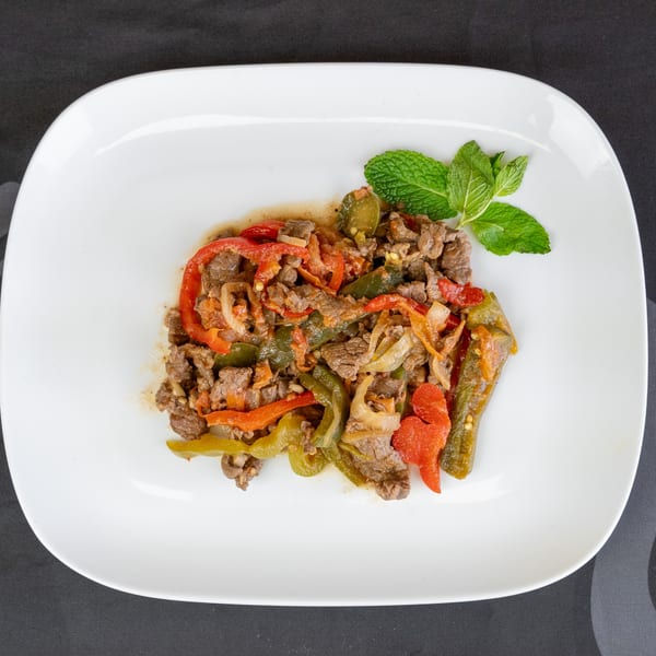 Sizzling beef fajitas with red and green bell peppers, onions, and a mint garnish on a white plate.