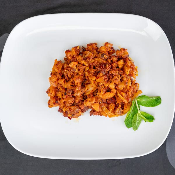 A white rectangular plate holds a serving of orange-brown diced potatoes and meat, garnished with mint.
