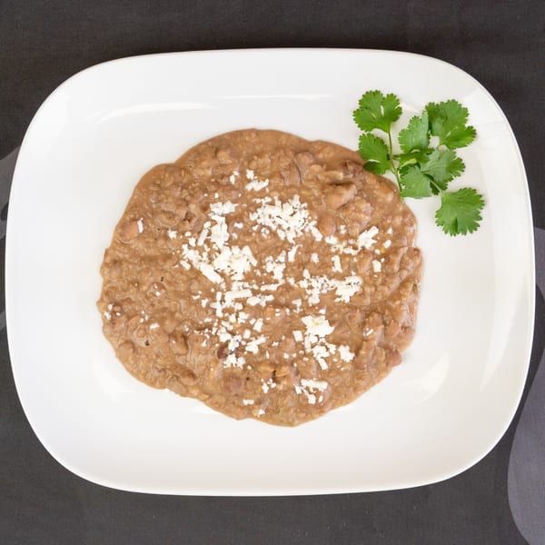 Refried beans topped with crumbled white cheese and a sprig of cilantro on a white plate.