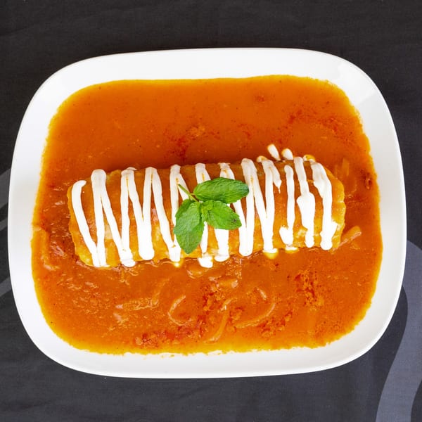 A white rectangular plate holds a burrito covered in red sauce, sour cream, and mint leaves.